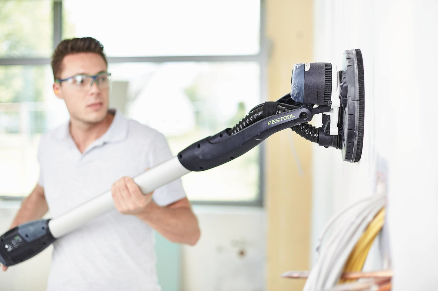 Man using Festool drywall sander with ergonomic handle for smooth wall sanding in power tools and woodworking collection