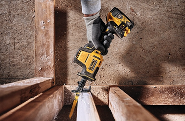 Person wearing glove operating DEWALT cordless one-handed reciprocating saw cutting wood beam in home improvement project