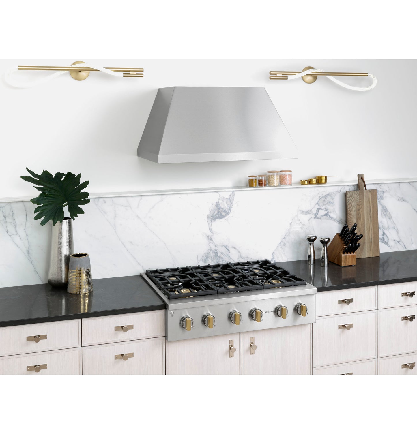 Stainless steel range hood above six-burner gas cooktop with marble backsplash and modern kitchen decor