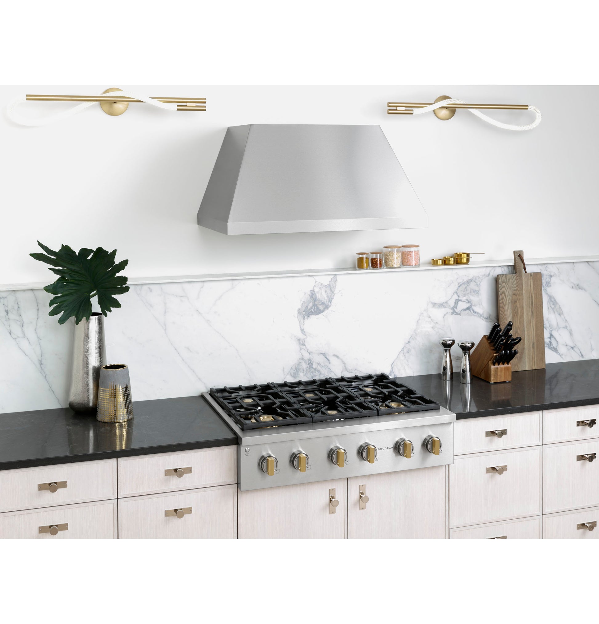 Stainless steel range hood above six-burner gas cooktop with marble backsplash and modern kitchen decor