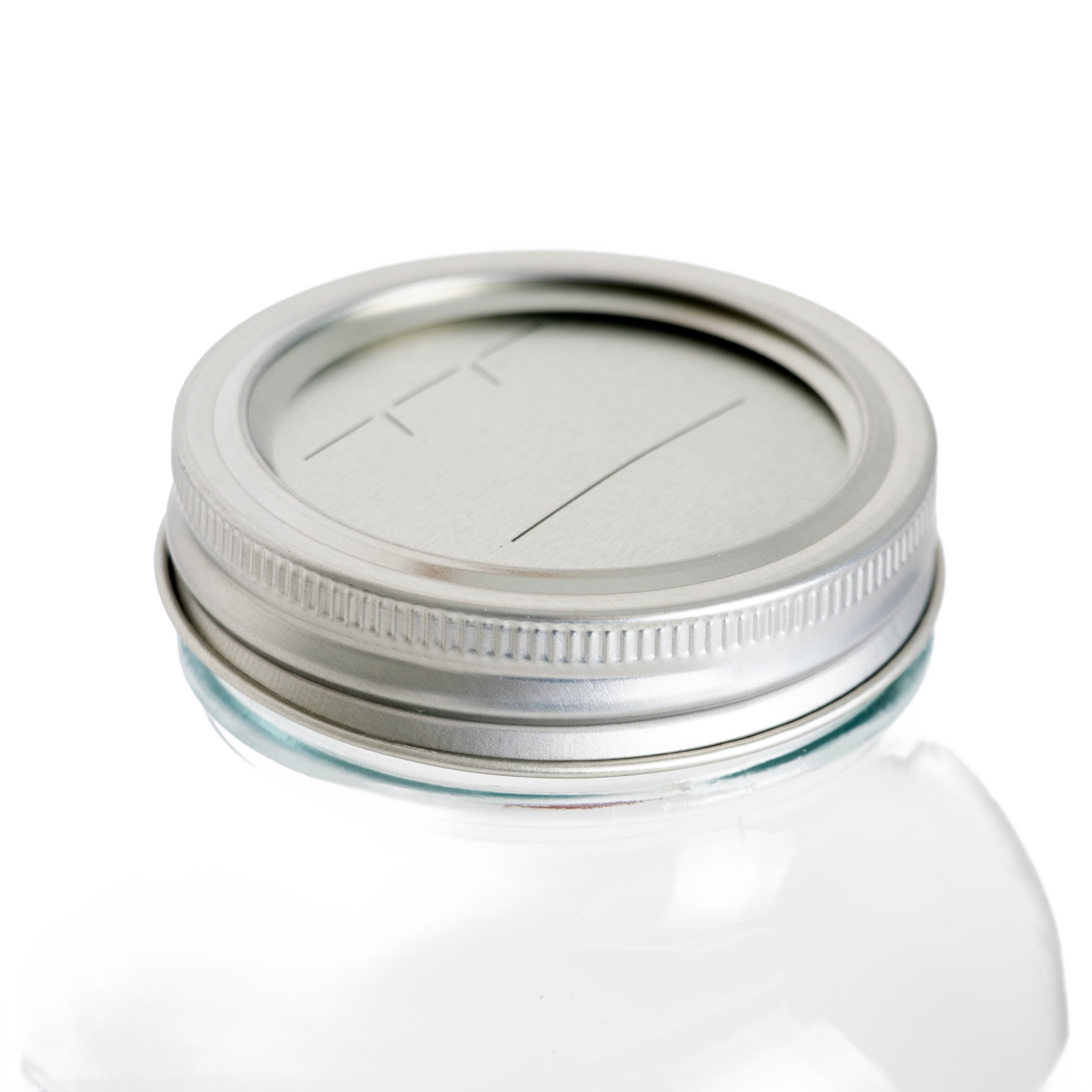 Close-up of silver-tone regular-mouth canning lid and band with date marking lines on clear glass jar in kitchenware collection