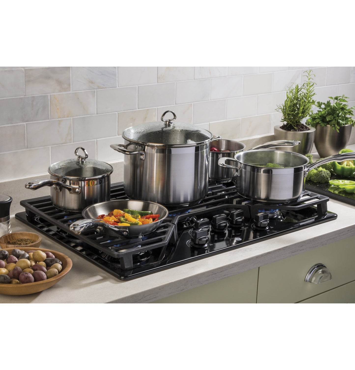 Black built-in gas cooktop with five burners cooking multiple stainless steel pots and pans in kitchen setting