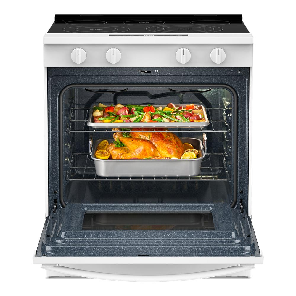 Open white electric range with two pans of roasted vegetables and a whole chicken cooking inside the oven cavity