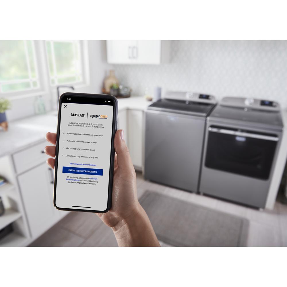 Hand holding smartphone displaying Amazon Dash setup app in laundry room with modern washer and electric dryer