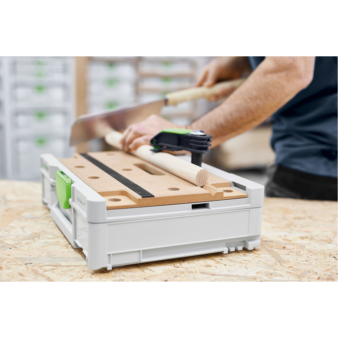 Compact Festool SYS3-MFT M 112 modular work surface with clamp securing a wooden dowel, used for precise cutting in a woodworking workshop setting.