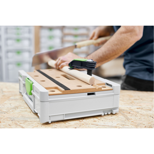 Compact Festool SYS3-MFT M 112 modular work surface with clamp securing a wooden dowel, used for precise cutting in a woodworking workshop setting.