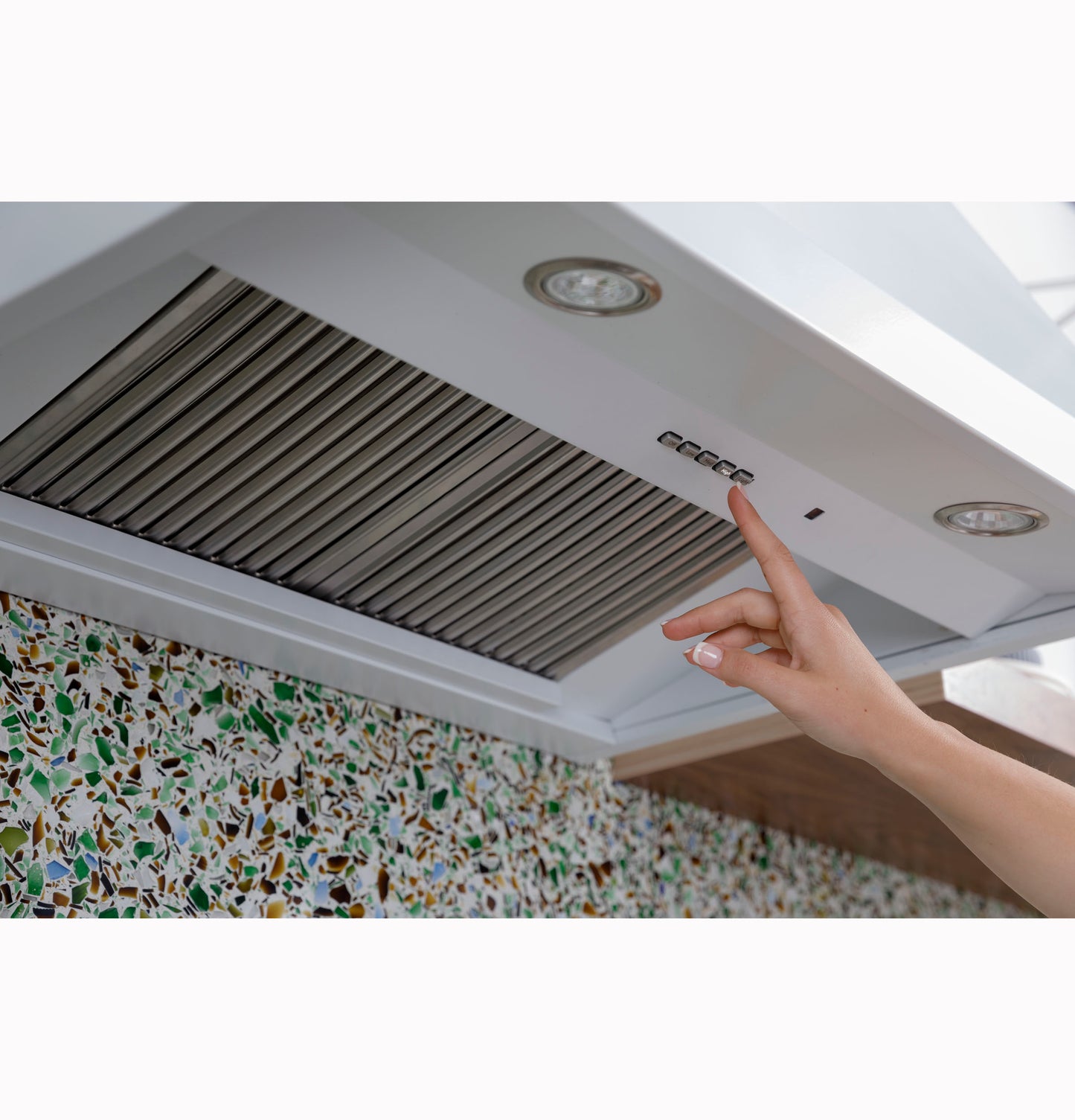 Hand pressing control buttons on white kitchen vent hood with stainless steel filters in home improvement setting