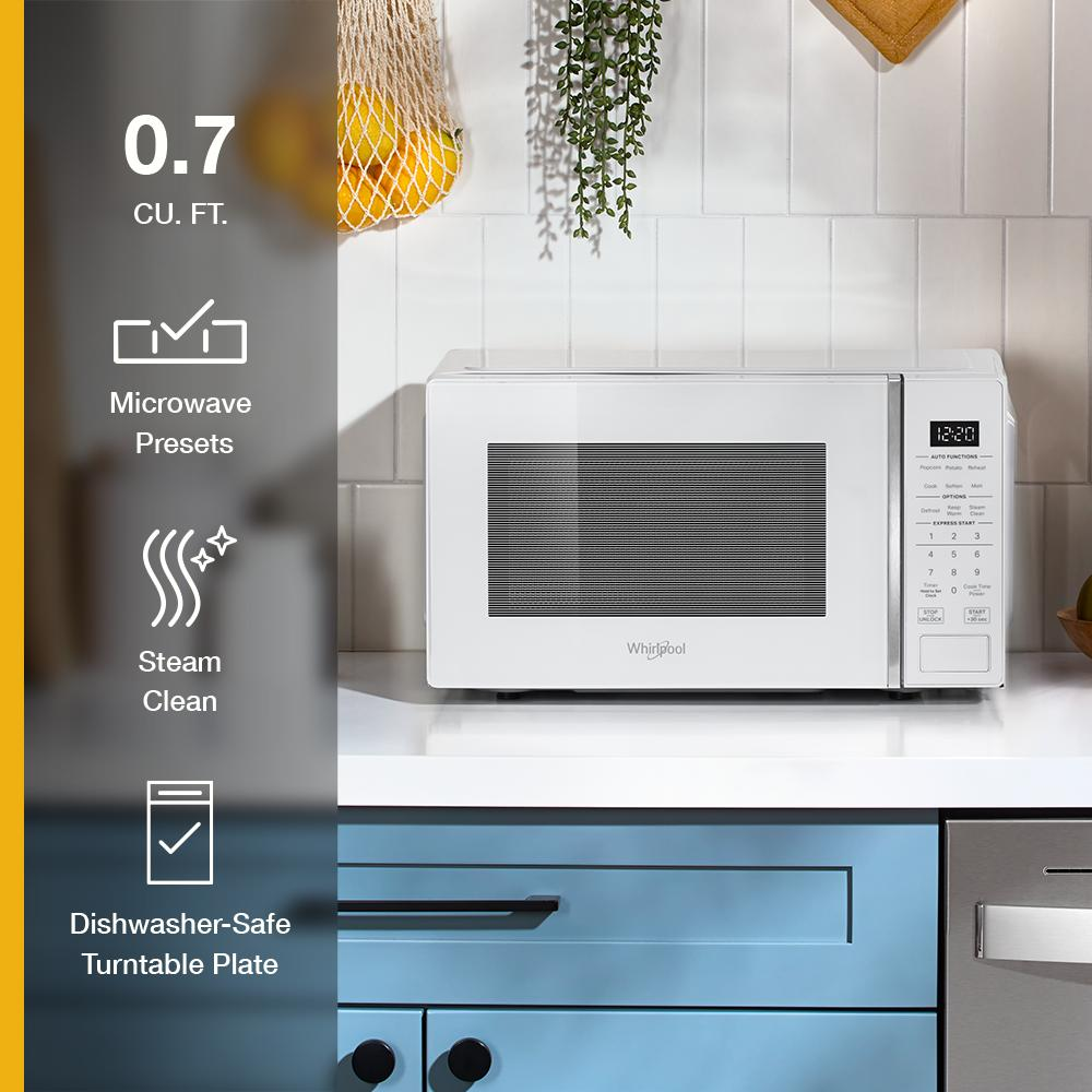 White countertop microwave with digital display and touch controls on kitchen counter with blue cabinets and plants