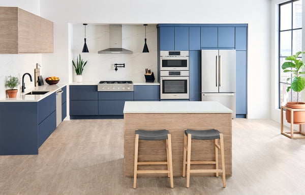 Contemporary kitchen featuring blue cabinetry, stainless steel appliances, and a wooden island with two stools in bright setting