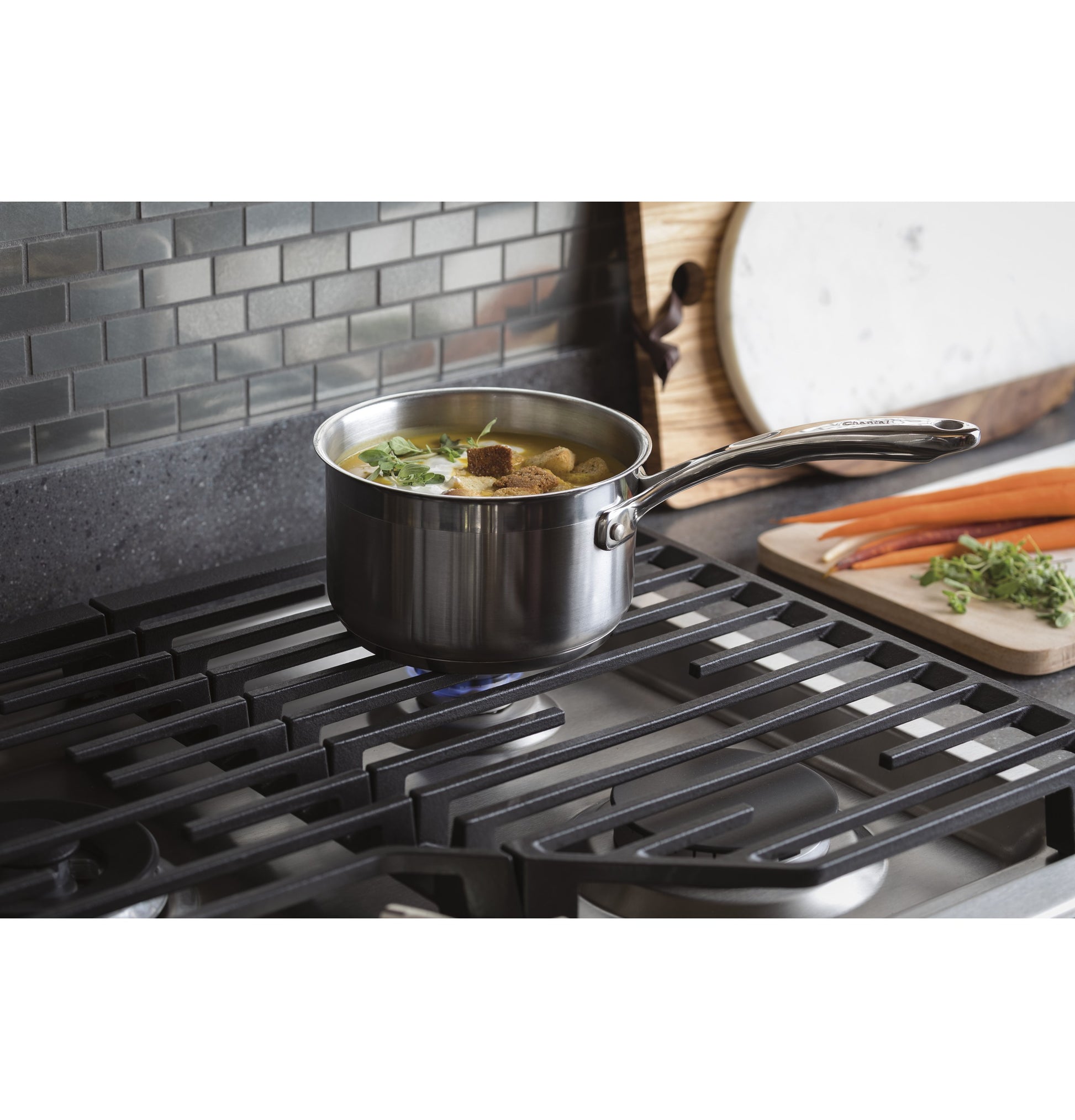 Stainless steel saucepan simmering soup on a modern gas cooktop with black grates and gray tiled backsplash