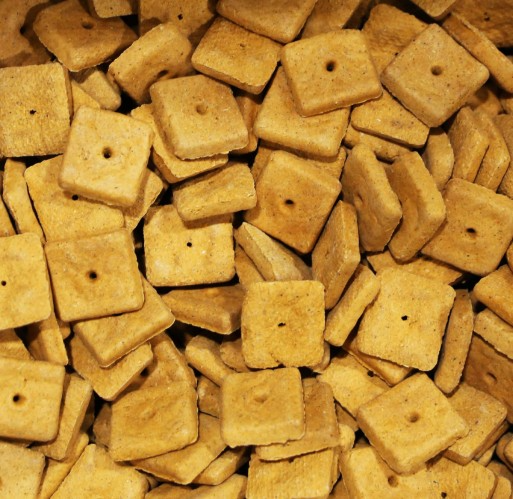 Close-up of square cheddar cheese-flavored dog treats with small hole in center, stacked closely together.