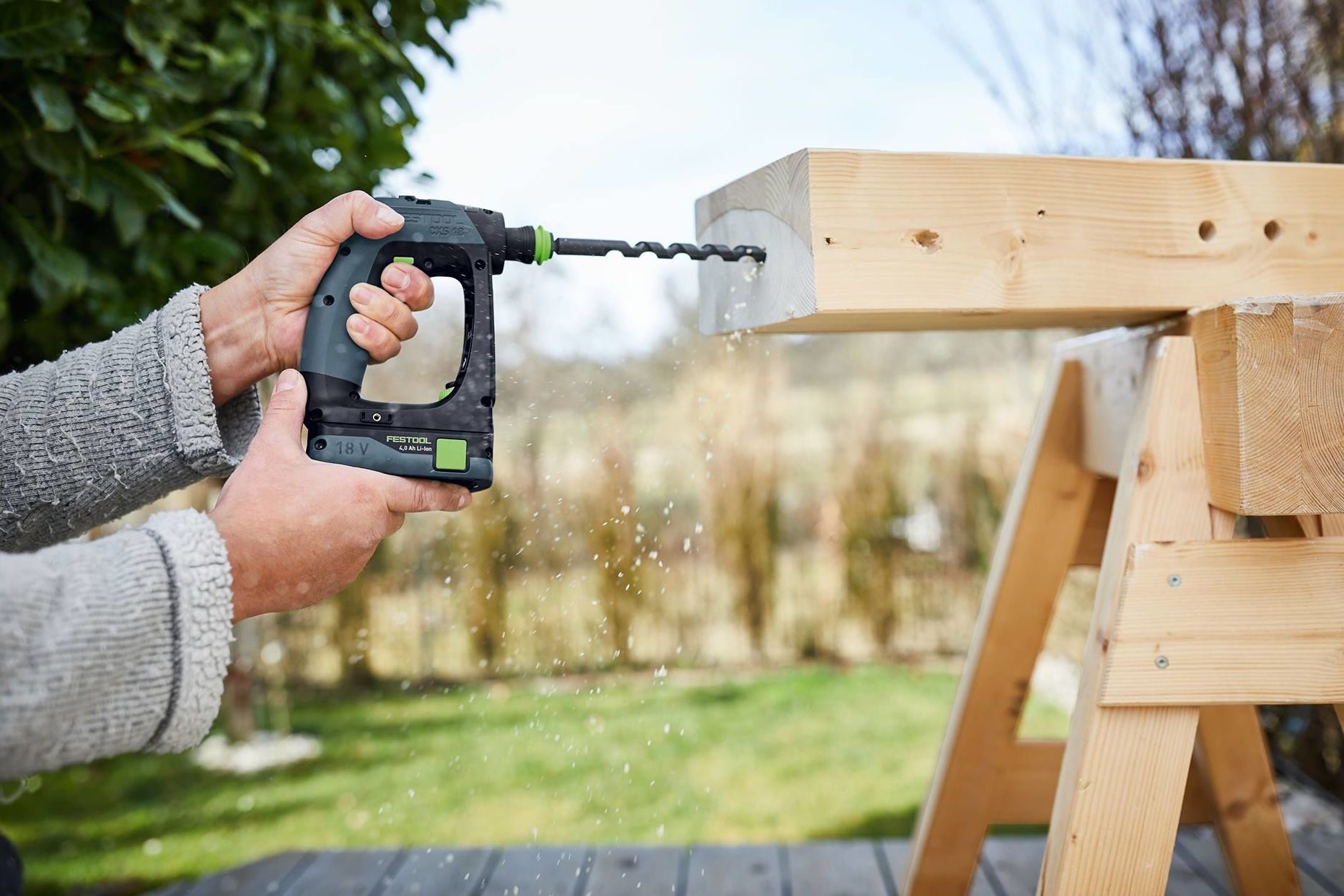 Person using compact cordless drill to bore holes into wooden beam outdoors in home improvement setting
