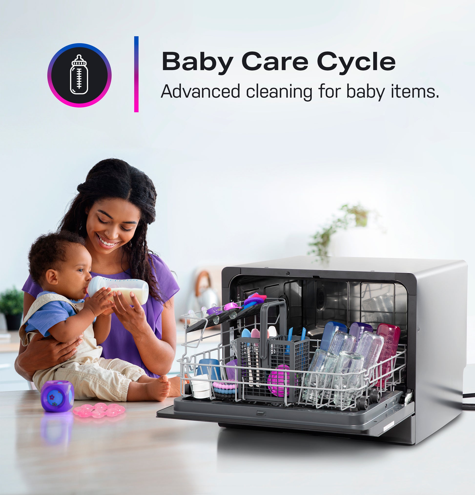 Compact dishwasher open with baby bottles inside and mother feeding infant in modern kitchen setting