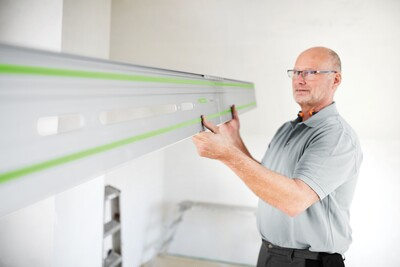 Man aligning a long Festool guide rail on a wall for precise woodworking and home improvement projects