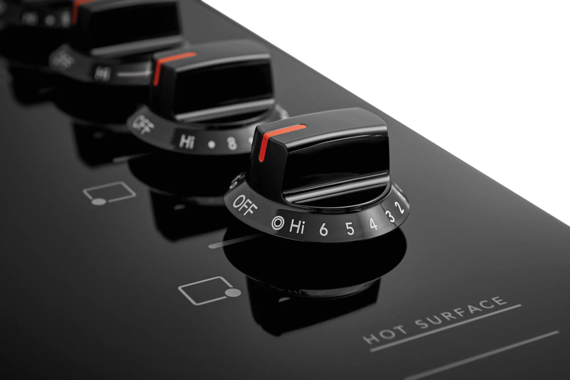 Close-up of black electric cooktop control knobs with heat settings and hot surface warning on smooth glass surface