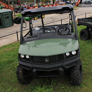 Green full-size crossover utility vehicle with roof and rugged tires parked outdoors on grass near equipment displays