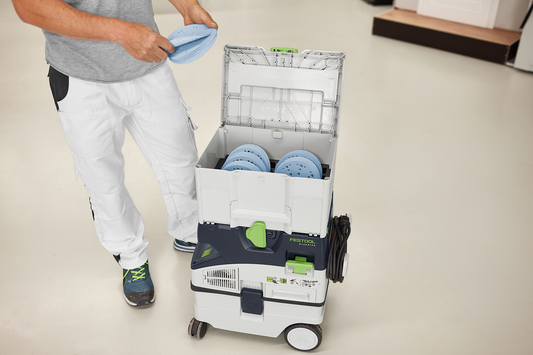 Person organizing blue sanding discs inside gray Festool abrasives storage case in a bright workshop setting