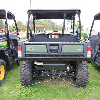 Rear view of green John Deere crossover utility vehicle with full roof, large tires, and cargo bed for outdoor use