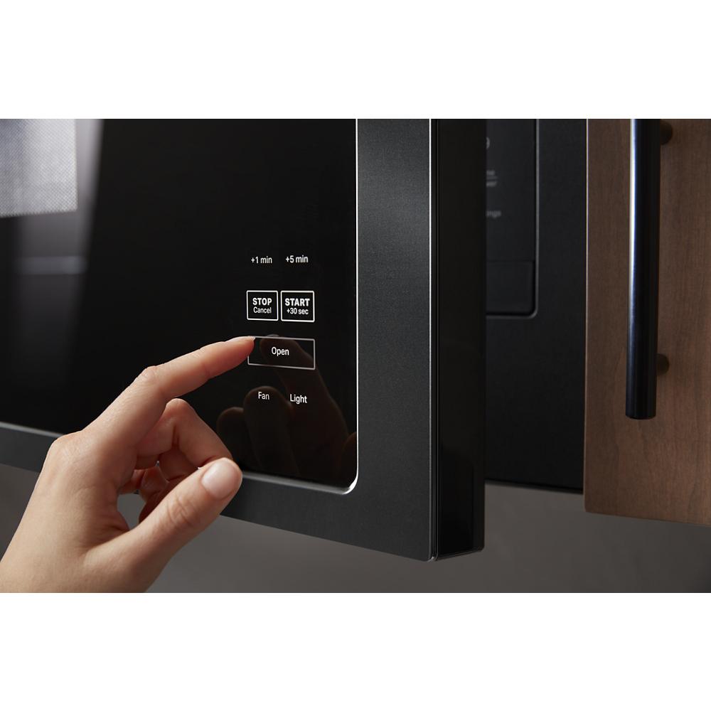 Hand pressing open button on black built-in microwave control panel in kitchen appliances setting