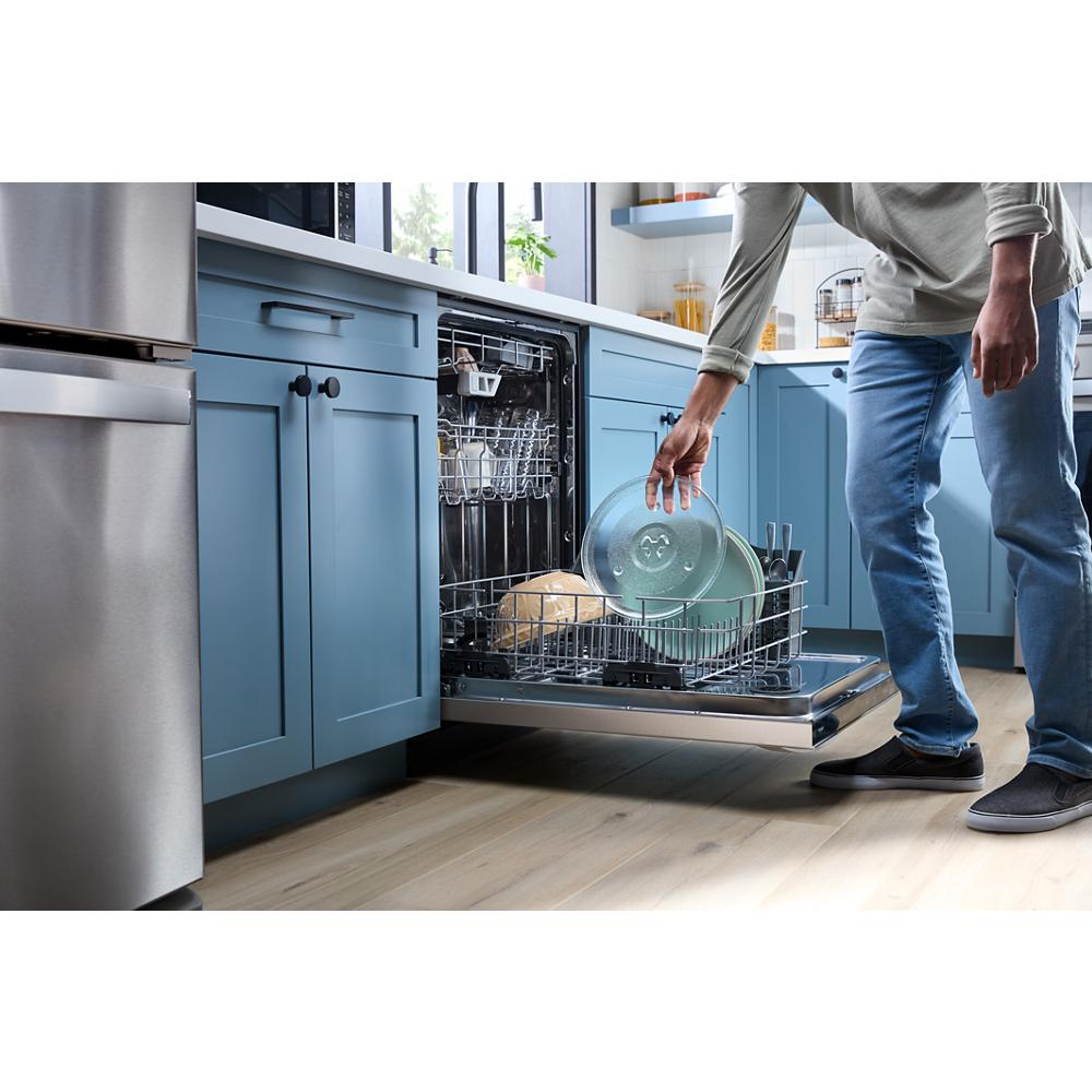 Person loading blue and beige dishes into lowered stainless steel built-in dishwasher in blue kitchen cabinetry setting