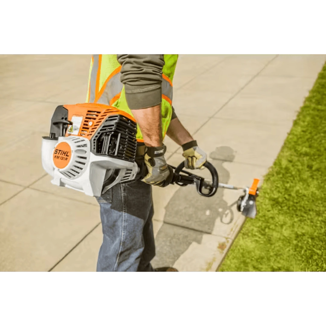 Person wearing work gloves and safety vest operating orange and white handheld KombiMotor tool for lawn edging in home improvement setting