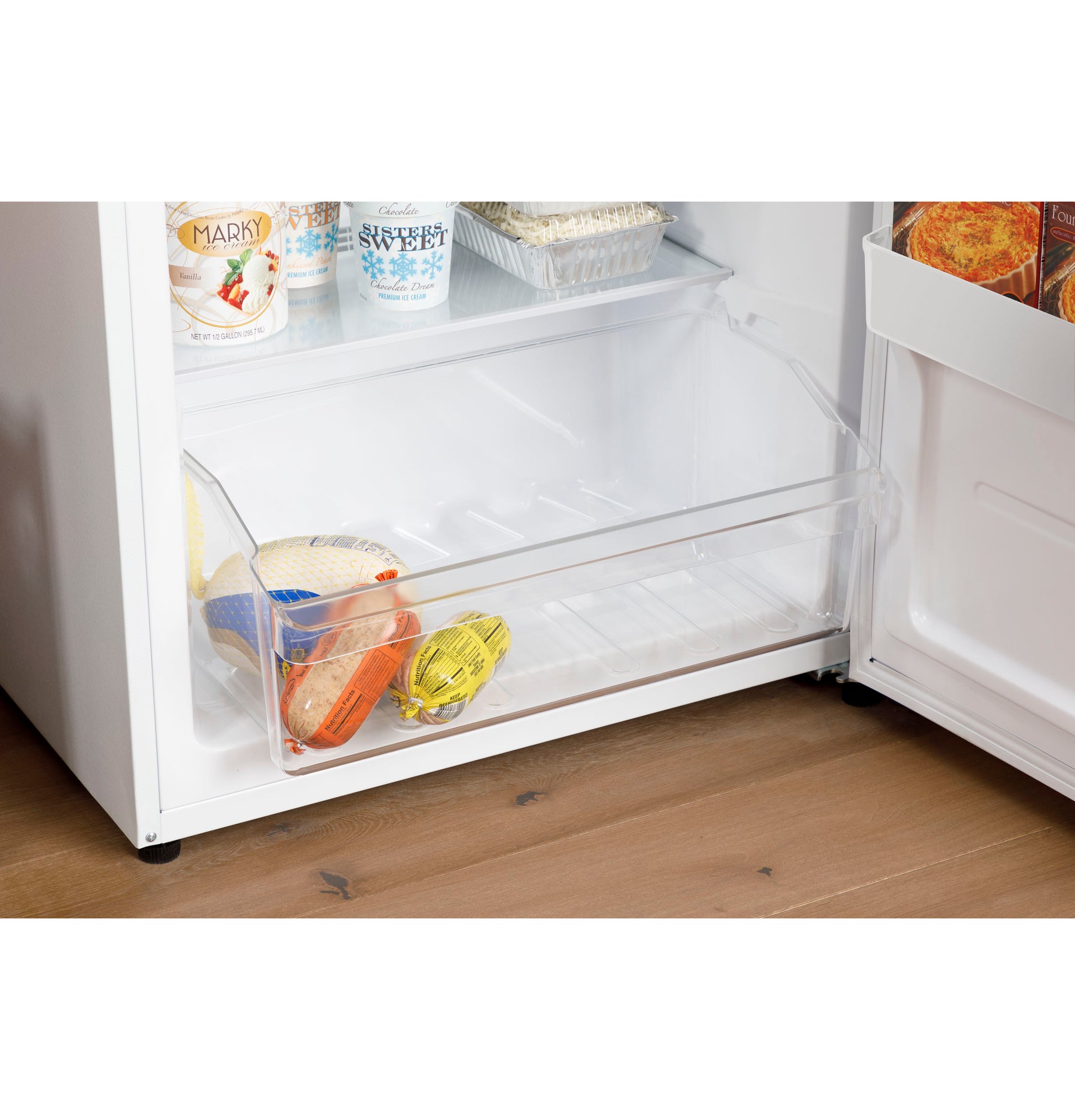 Clear lower freezer drawer inside frost-free upright freezer with packaged frozen foods on wooden kitchen floor
