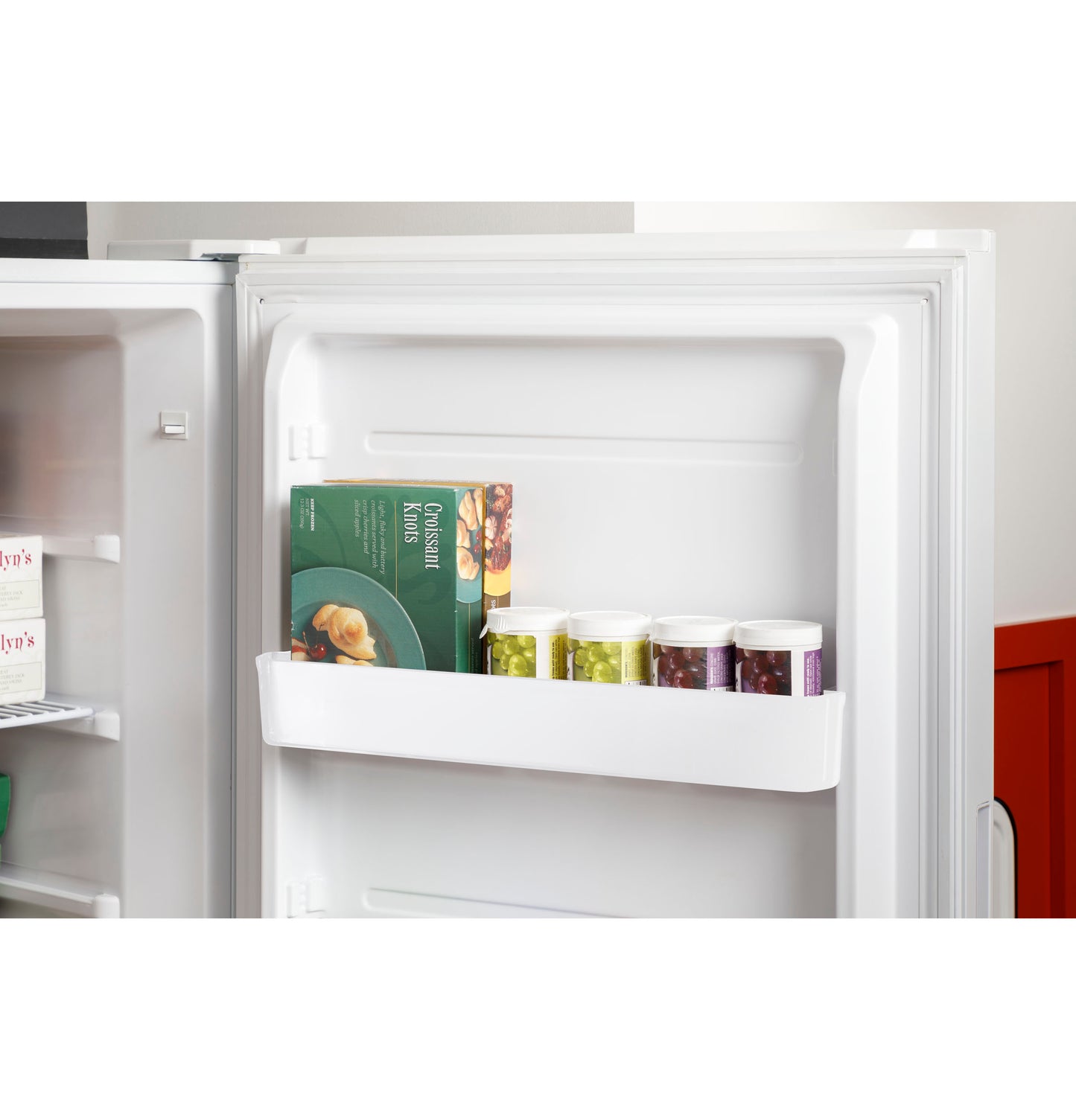 Open door of white upright freezer showing door shelf stocked with frozen food and packaged goods in kitchen
