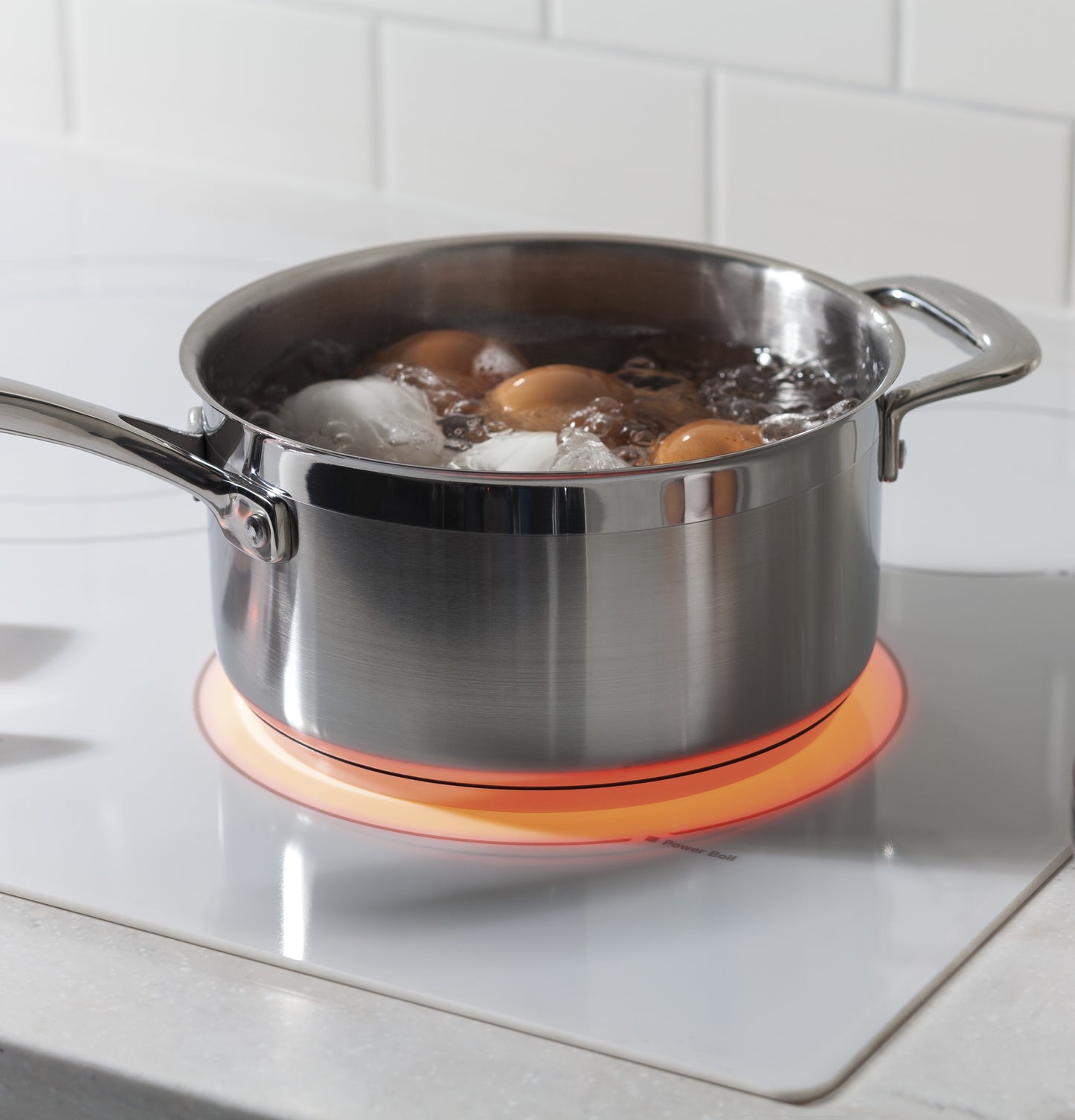 Stainless steel pot boiling eggs on white electric cooktop surface glowing red burner in kitchen setting