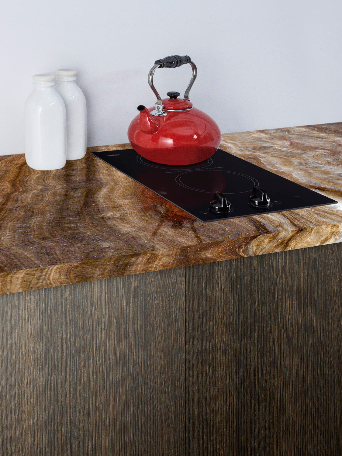 Black 12-inch radiant cooktop with two burners installed in a wood grain countertop next to white ceramic bottles