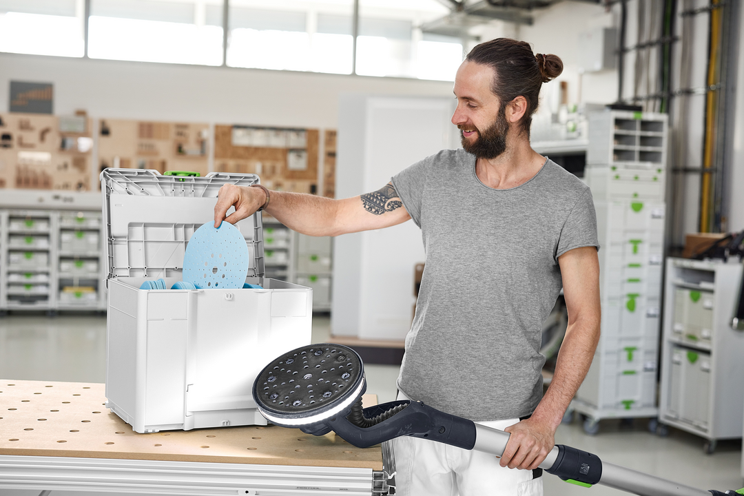Man with long hair holding a sander and placing abrasive discs into a Festool Granat abrasives Systainer in workshop