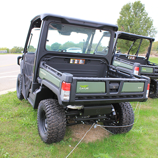 Rear view of green utility vehicle with cargo bed and rugged tires parked on grass field outdoors