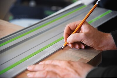 Hand marking wood edge along a Festool guide rail with green anti-slip strip for precise woodworking tools accessory use