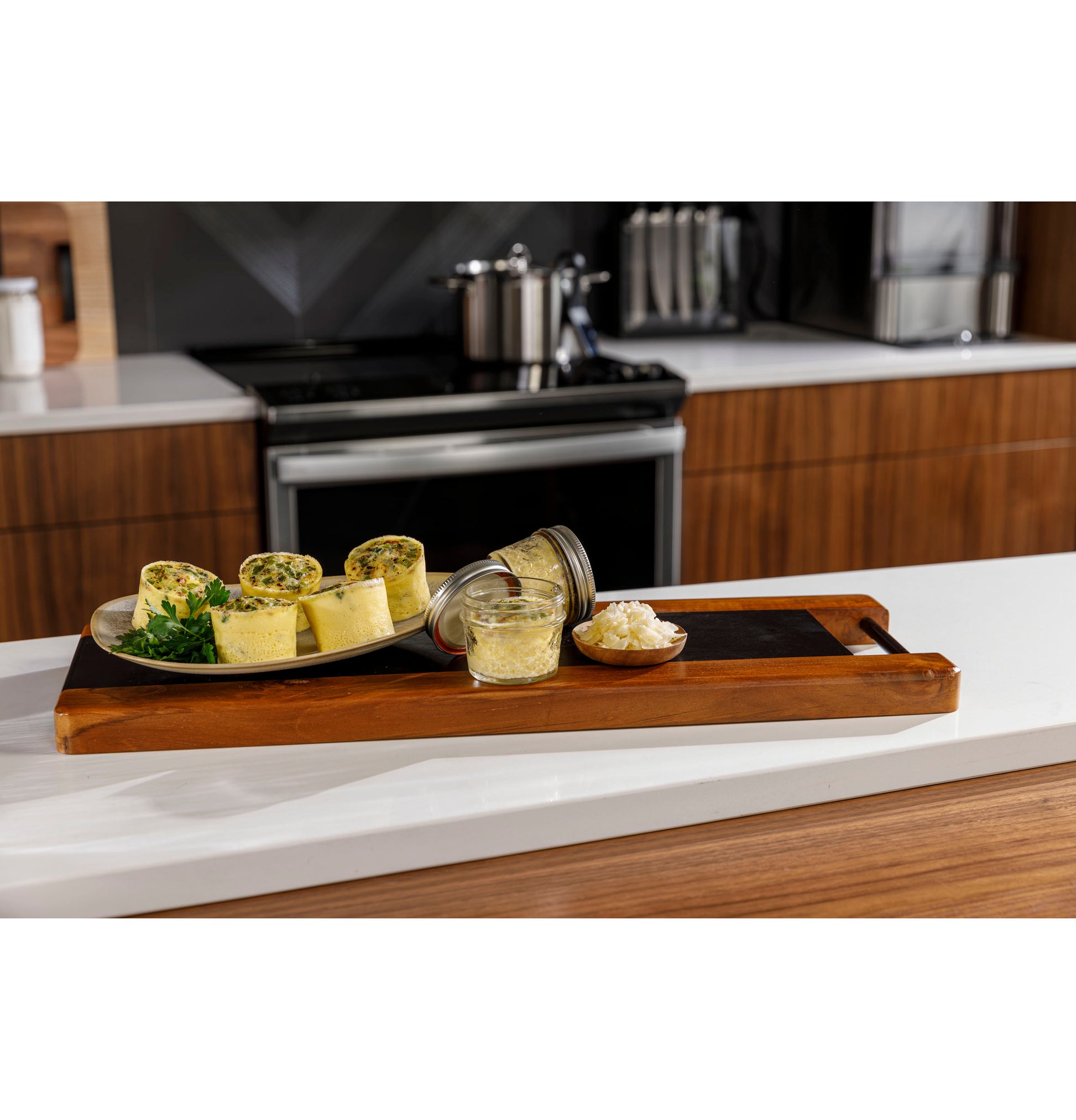 Plate of savory egg rolls with herbs and small jars of ingredients set on wooden tray on modern kitchen counter