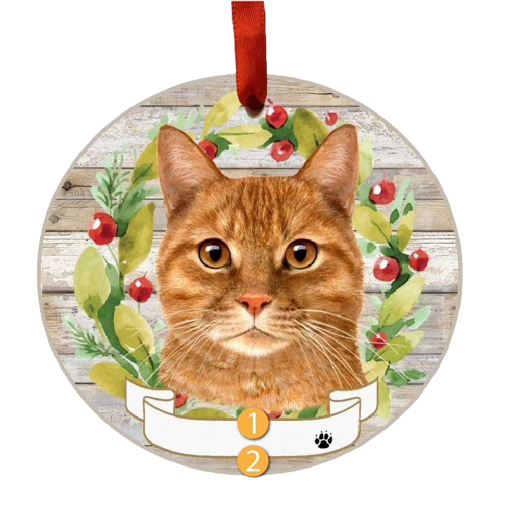 Round Christmas ornament with orange tabby cat face and festive wreath of leaves and red berries decoration