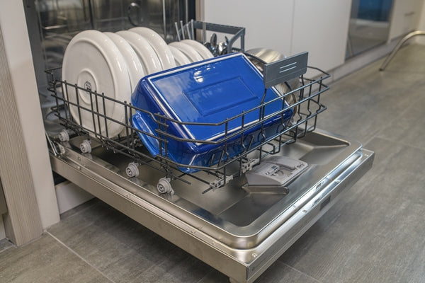 Open drawer of 24-inch dishwasher loaded with plates and blue cookware inside modern kitchen appliance