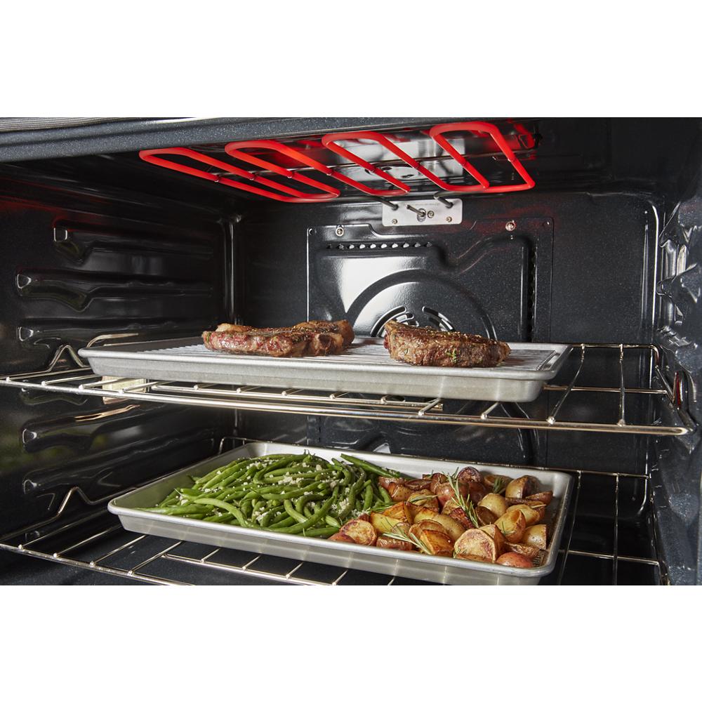 Interior view of single wall oven with two racks cooking steak, green beans, and roasted potatoes in kitchen appliances collection