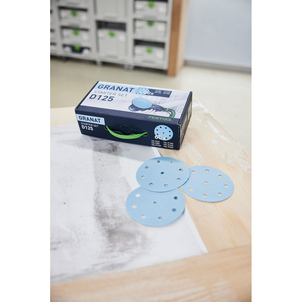 Box of Festool Granat D125 sanding discs with three blue perforated abrasives on wood surface in workshop setting