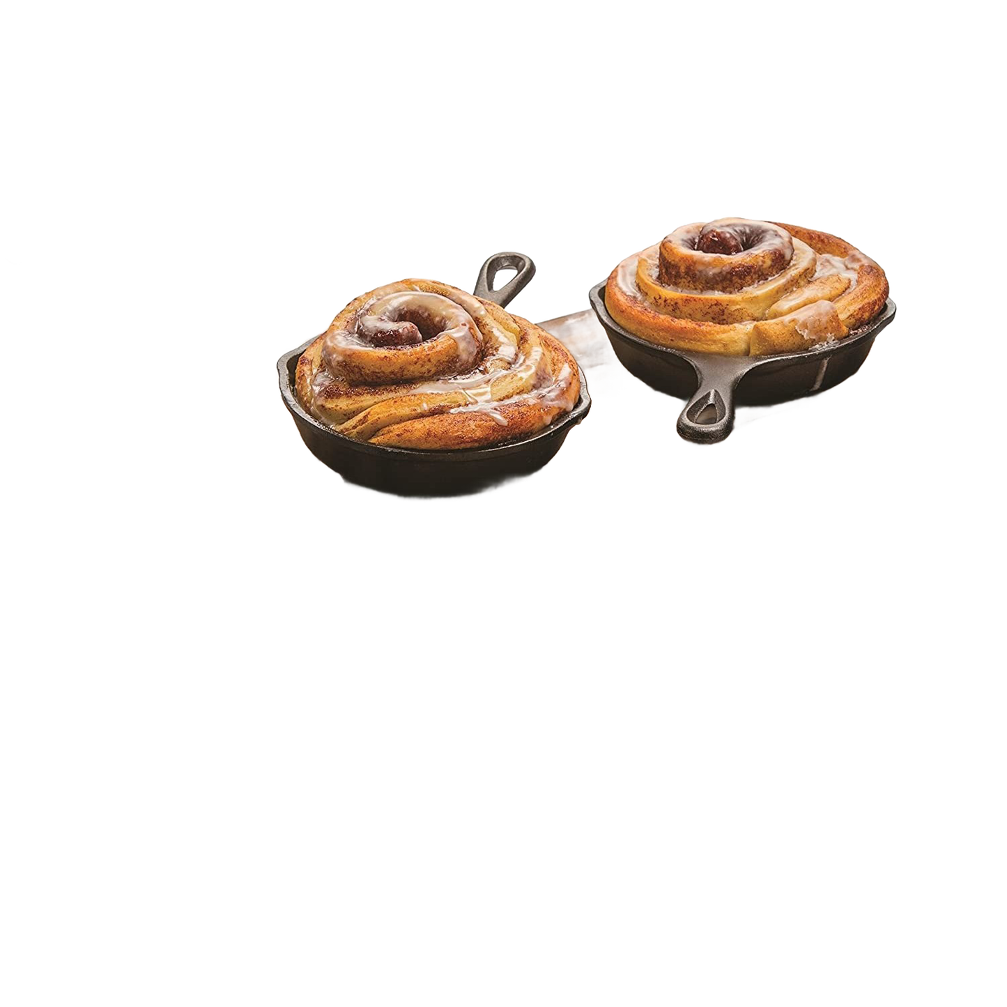 Two mini cast iron skillets each holding a freshly baked cinnamon roll on wooden board in kitchenware setting