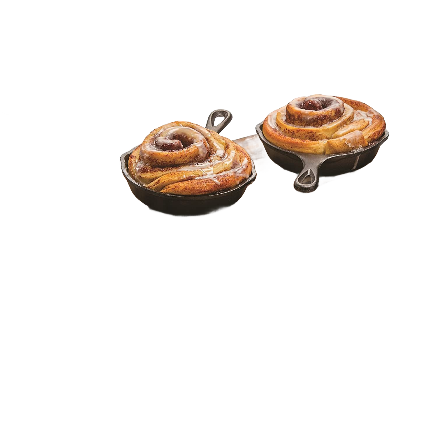 Two mini cast iron skillets each holding a freshly baked cinnamon roll on wooden board in kitchenware setting