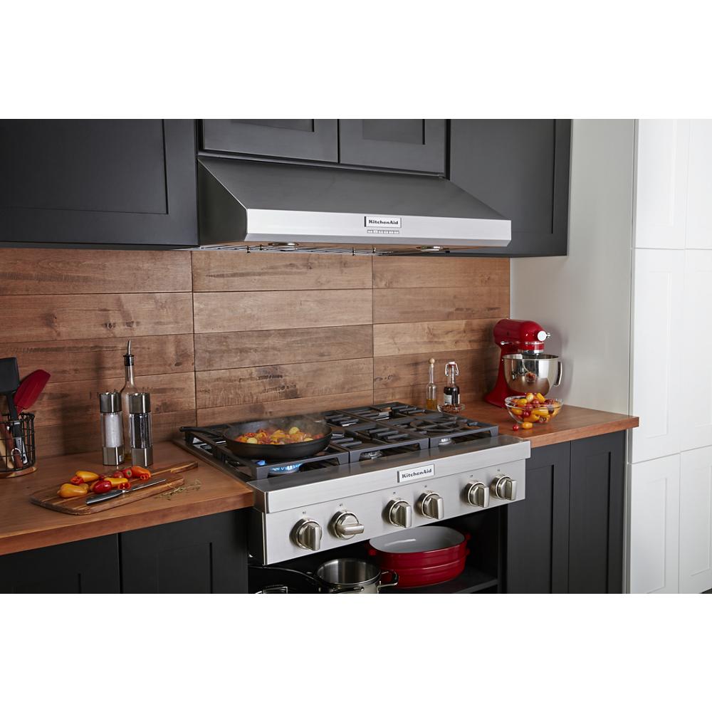 Stainless steel 6-burner commercial-style gas cooktop with control knobs in modern kitchen setup with wooden backsplash