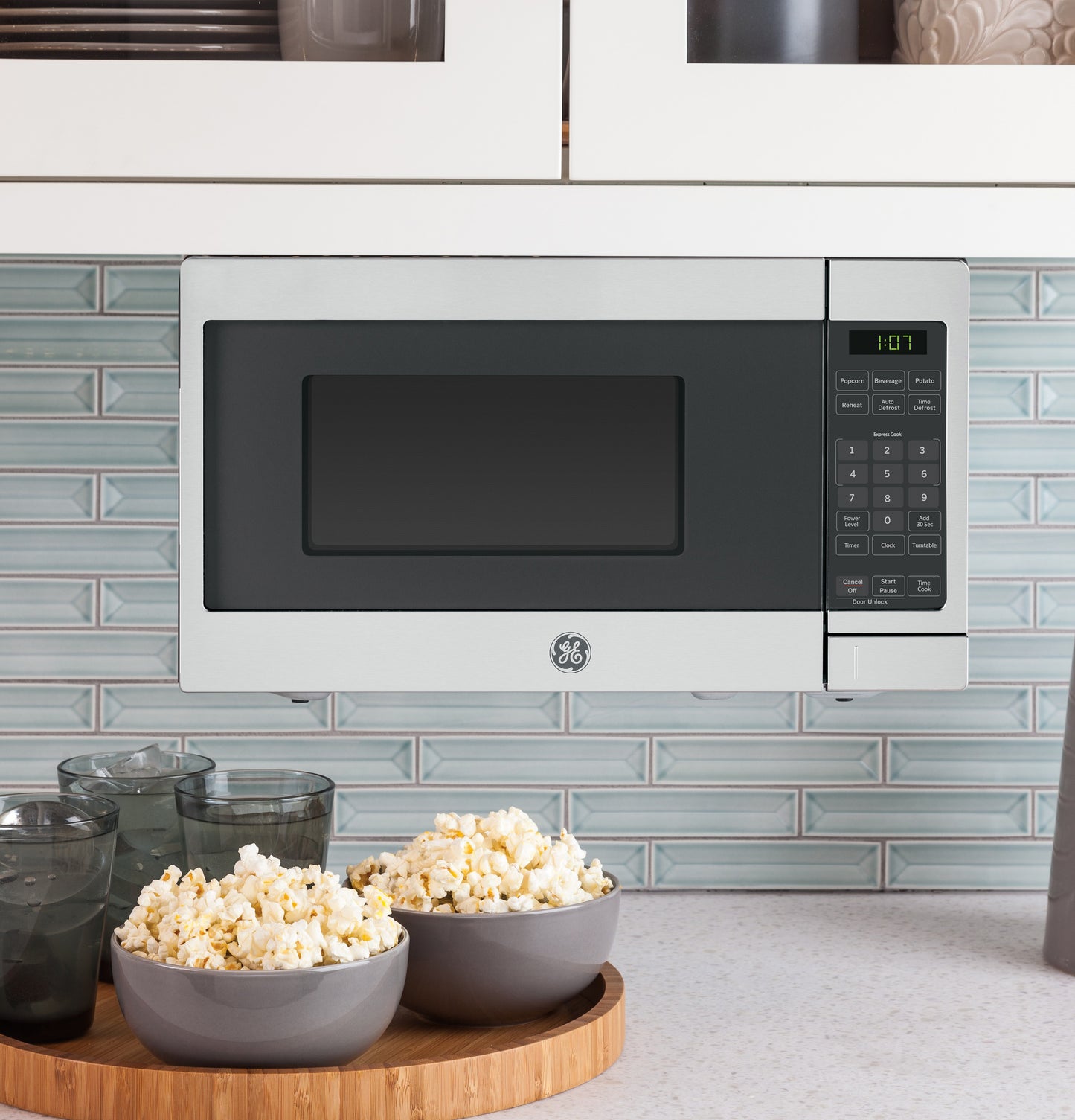 Stainless steel Spacemaker microwave mounted above countertop with bowls of popcorn and glass cups nearby in kitchen setting