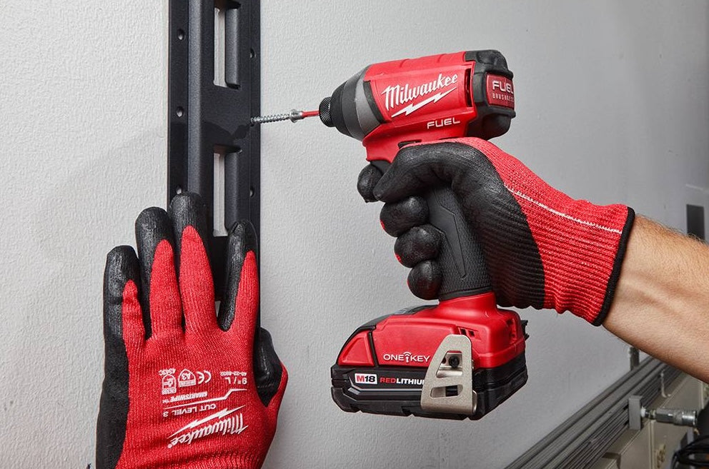 Worker wearing red gloves using a cordless drill to install heavy-duty vertical steel E-Track shelving for wall storage