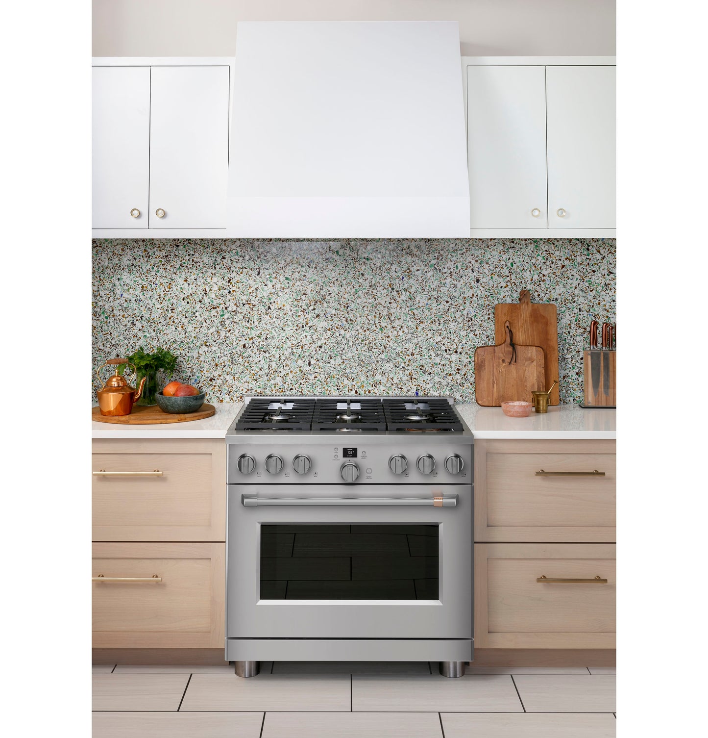 Stainless steel six-burner gas range with digital controls in a modern kitchen with terrazzo backsplash and light wood cabinets