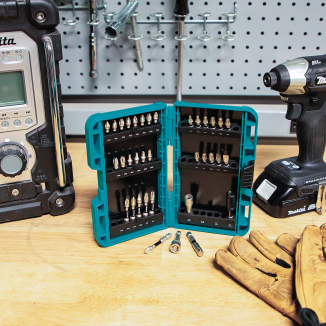 Teal impact bit set case open showing assorted bits with power tools and work gloves on wooden bench for home improvement