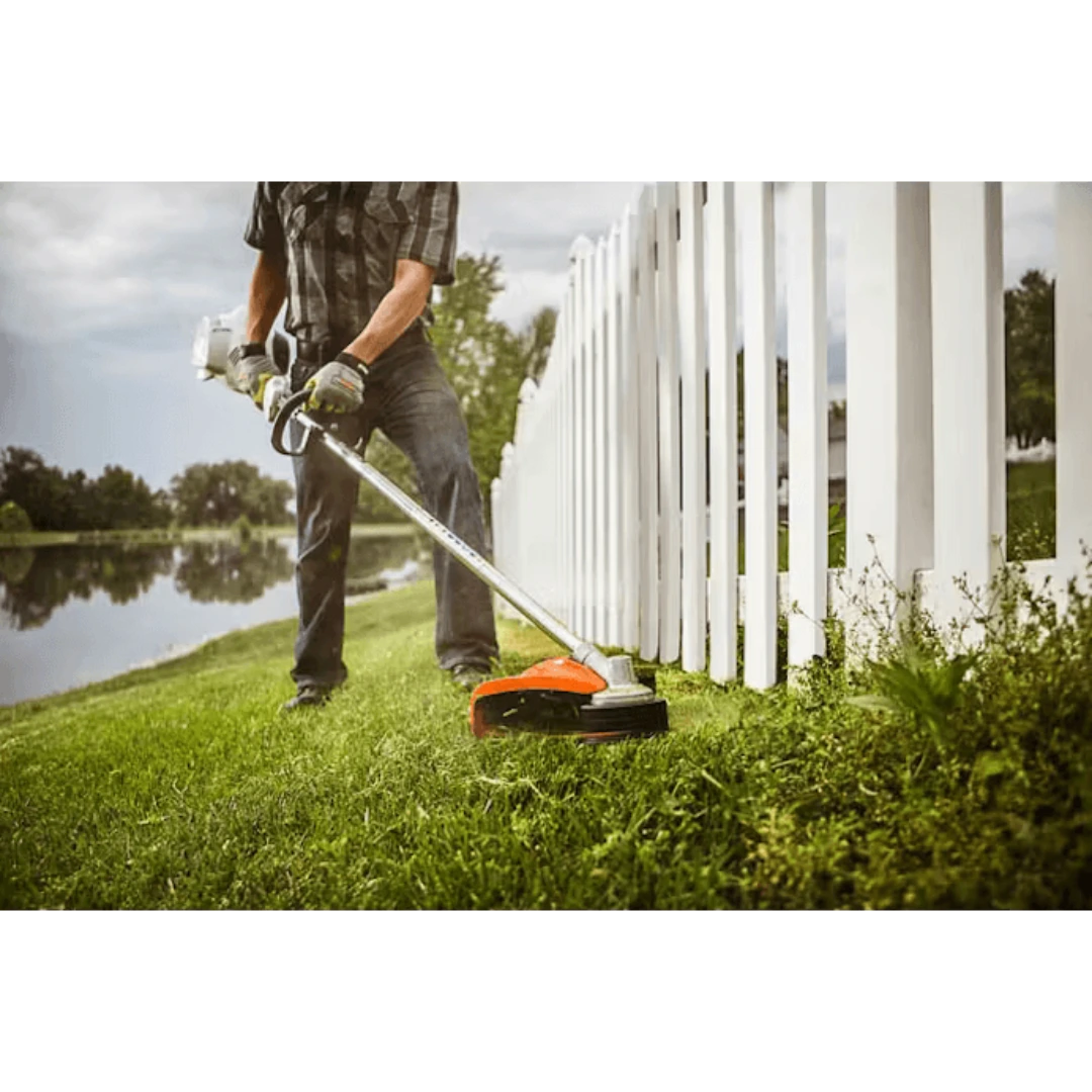 Person trimming grass near white fence using straight shaft trimmer with bike-handle for home improvement tasks