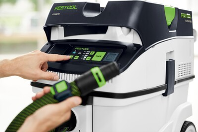 Close-up of hand adjusting control panel on Festool Cleantec dust extractor amid woodworking tools and air filtration equipment