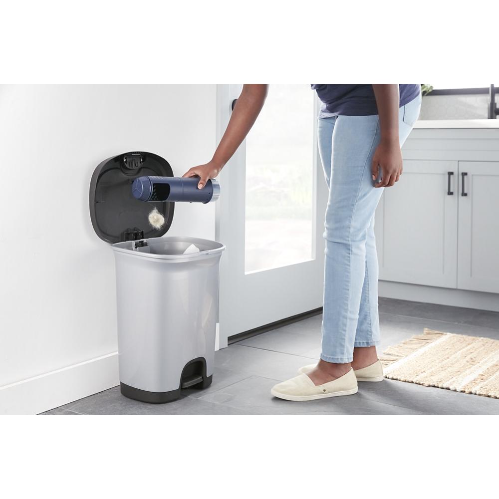 Person emptying lint trap from silver dryer into stainless steel trash can in bright laundry room with white cabinetry