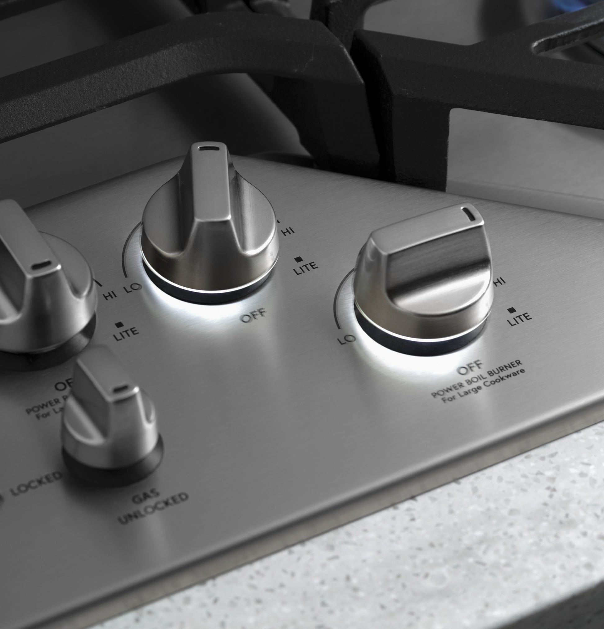 Close-up of stainless steel gas cooktop control knobs with black grates from Cooktops and Kitchen & Kitchenware collections