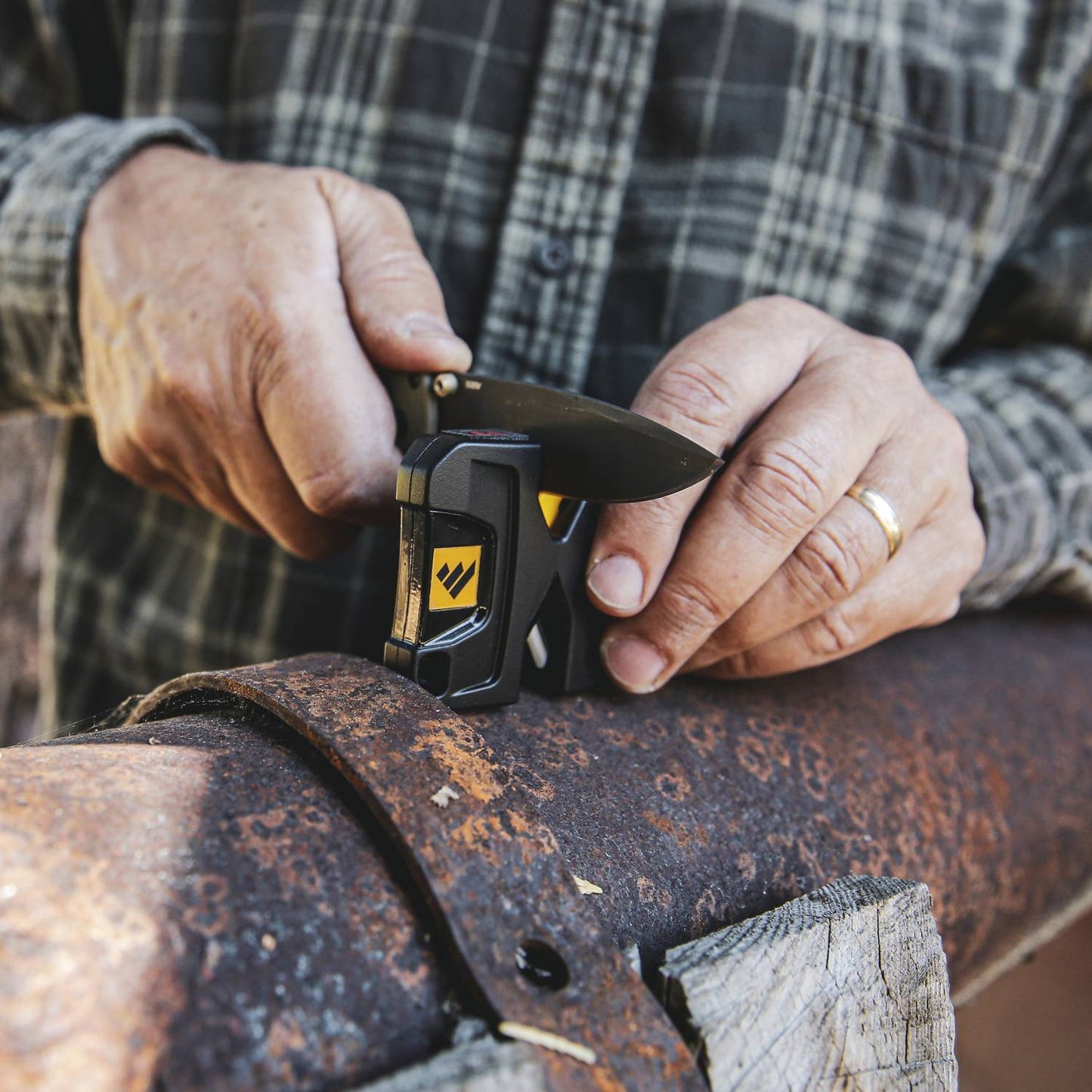 Person using black and yellow handheld pivot knife sharpener on folding knife outdoors for tools maintenance