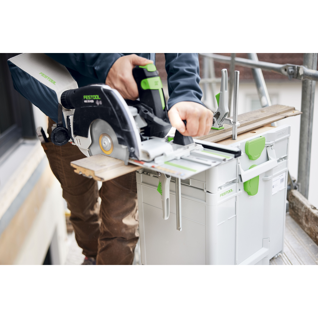 Person operating a Festool circular saw mounted on an interlocking SYS3-MFT M 112 modular work surface with tool storage on a construction site.